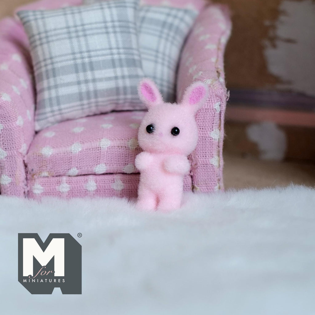 1:12 scale miniature sitting bunny doll in pink flocked finish with long ears, on a white fluffy rug by a pink armchair
