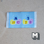 1:12 scale miniature letter blocks rug in light blue with ABC and 123 toy block print, shown on a board