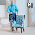1:12 scale miniature resin George III style armchair with blue floral needlepoint upholstery, shown beside a poseable figure