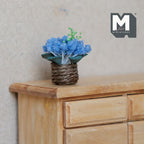 1:12 scale miniature blue flowers with green leaves in a brown twine pot, shown on a light wood dresser