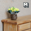 1:12 scale miniature yellow flowers with green leaves in a brown twine pot, shown on a light wood dresser