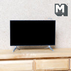 1:12 scale miniature flat screen TV in black with stand feet, non working, shown on a wood TV cabinet