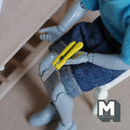 1:12 scale miniature metal utility knife with retracting blade in yellow, non working, shown held by a poseable figure