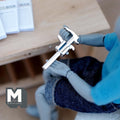 1:12 scale miniature metal vernier caliper in silver with printed scale, non working, held by an artist figure