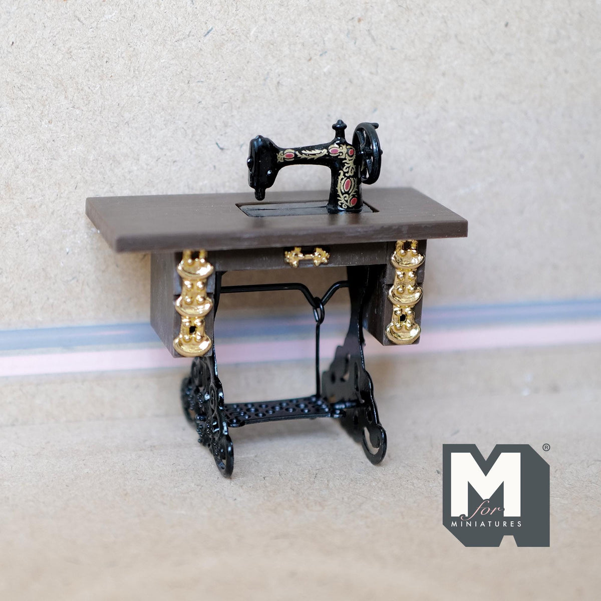 1:12 scale miniature treadle sewing machine in black with gold detail on a table with an iron look base