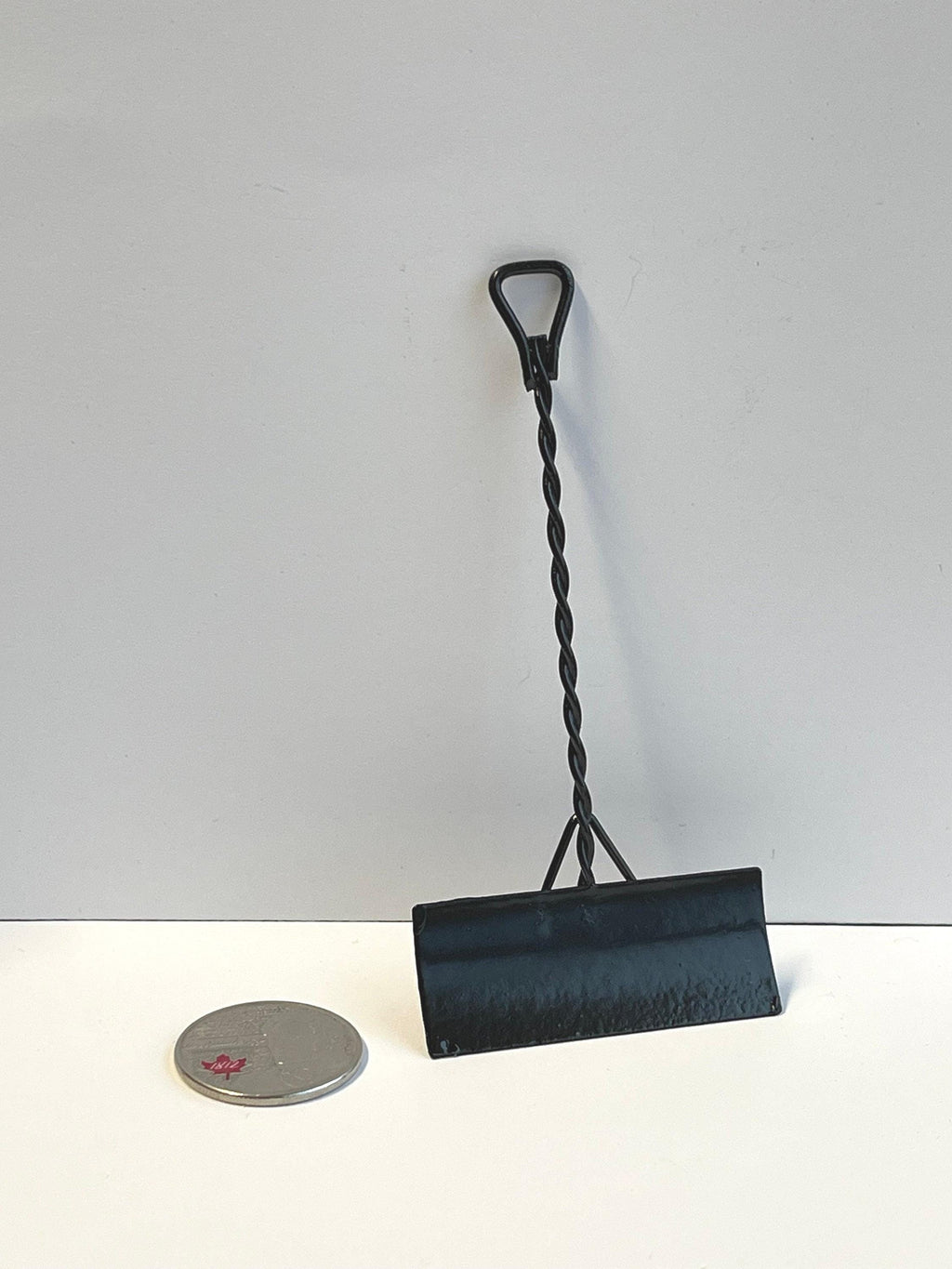 1:12 scale miniature black metal snow shovel with twisted handle and D grip, shown standing beside a coin for scale