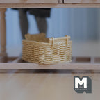 1:12 scale miniature resin rattan style basket in beige with two handles, shown on a low wood shelf