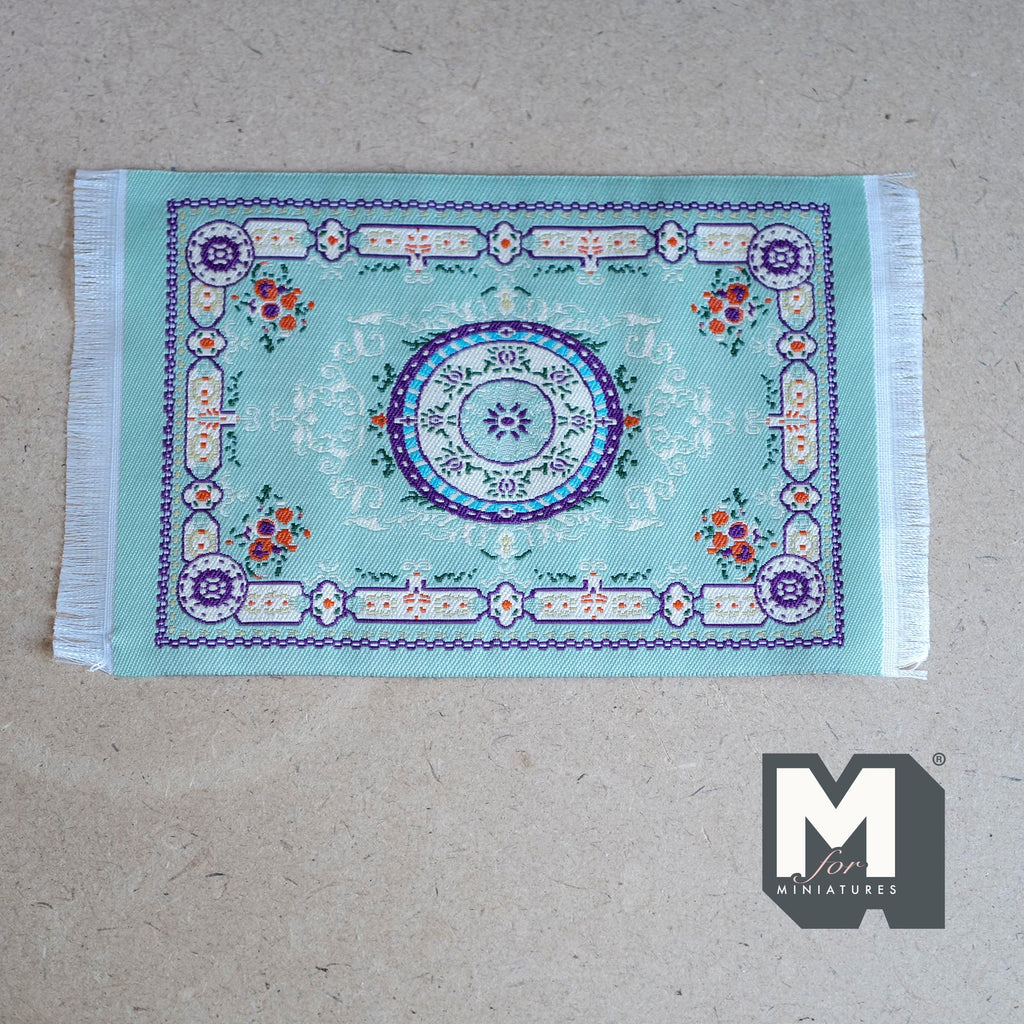 1:12 scale miniature medallion area rug in mint green with fringe and floral corners, shown flat on a gray floor