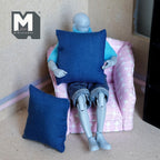 1:12 scale miniature fabric square cushions in dark blue, set of 2, shown with a poseable figure on a pink chair