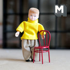 1:12 scale miniature metal wire back kids chair in red, shown beside a child doll in a yellow sweater
