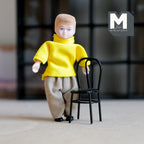1:12 scale miniature metal wire back kids chair in black, shown beside a child doll in a yellow sweater