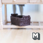 1:12 scale miniature rattan style resin basket in dark brown with handles, shown under a wood table
