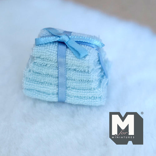 1:12 scale miniature bath towel stack in blue tied with a ribbon bow, set of 6, shown on a white fur rug