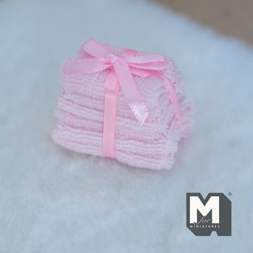 1:12 scale miniature bath towel stack in pink, set of 6, tied with a pink satin ribbon bow, shown on a white fluffy rug