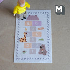 1:12 scale miniature beige printed hopscotch play rug with animals and alphabet letters, shown with a toy figure