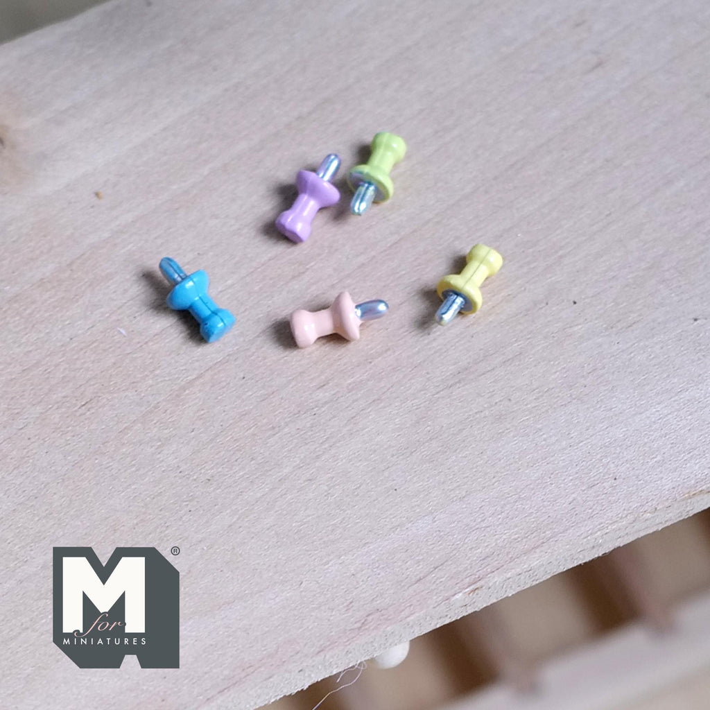 1:12 scale miniature push pins in assorted pastel colors, set of 5, scattered on a light wood surface