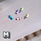 1:12 scale miniature push pins in assorted pastel colors, set of 5, scattered on a light wood surface