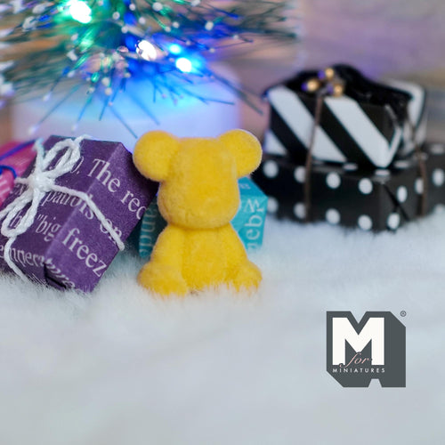1:12 scale miniature bear cub in yellow with flocked skin, shown from behind among gift boxes under a tree