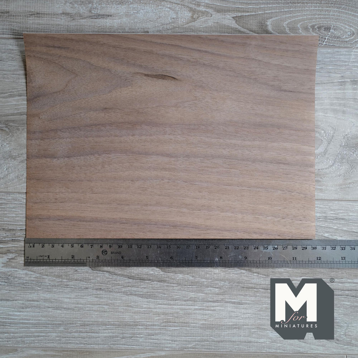 Miniature walnut peel and stick wood veneer sheet, dark brown natural grain, shown with a ruler on a gray wood surface