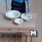 1:12 scale miniature metal bowls with beaded rim in yellow, set of 3 nesting sizes, on a wood table with a poseable figure