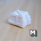 1:12 scale miniature stack of 6 folded towels in white tied with a white ribbon, shown on a wood surface