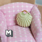 1:12 scale miniature knitted handbag in green with gold handles, shown on a pink polka dot armchair