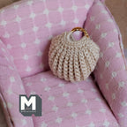 1:12 scale miniature knitted handbag in beige with gold handles, shown on a pink polka dot armchair