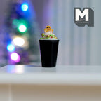 1:12 scale miniature midnight gingerbread latte in a black cup with cream and a gingerbread man, shown on a white table