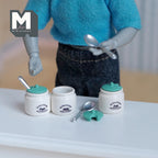 1:12 scale miniature metal kitchen storage jars with spoons, 3 white jars with green lids, shown on a white table
