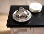 1:12 scale miniature small round serving tray with dome cover in silver, set of 2, shown on a black countertop