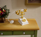 1:12 scale miniature French style dial telephone in white and gold with a curly cord, shown on a wood side table