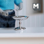 1:12 scale miniature metal pedestal cake stand, medium, in shiny silver with a turned stem, shown on a white table