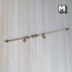 1:12 scale miniature brass curtain rod in gold with 10 rings and 2 hangers, fixed length, shown on a wood surface