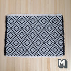 1:12 scale miniature geometric diamond woven rug with fringe in black and white, shown flat on a wood floor