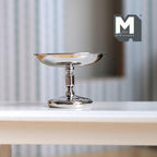 1:12 scale miniature metal pedestal cake stand, tall, in shiny silver with a turned stem, shown on a white shelf