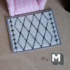 1:12 scale miniature diamond trellis shag area rug in white and black with arrow lines, shown by a pink armchair