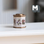 1:12 scale miniature octagonal floral tea tin with lid in cream with purple and red flowers, shown on a white shelf