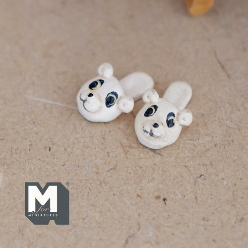 1:12 scale miniature resin bear face slippers in white with black eyes and round ears, pair shown on a brown floor