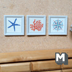 1:12 scale miniature coastal wall art prints, starfish, coral and compass, set of 3 in white frames, shown hung on a wall