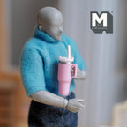 1:12 scale miniature tumbler with straw and handle in pink, held by a posable figure in a blue sweater