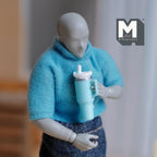 1:12 scale miniature tumbler with straw and handle in aqua blue, held by a posable figure in a blue sweater