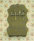 1:12 scale miniature spoon rack wall kit in tan with four hanging spoons and a lower box, shown against floral wallpaper