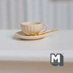 1:12 scale miniature scalloped cup, saucer and spoon set in beige with a gold spoon, set of 3, shown on a white table