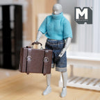 1:12 scale miniature faux leather suitcase with straps in brown, non opening, shown carried by an artist figure