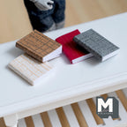 1:12 scale miniature books with blank pages, set of 4 with brown, red, gray and white fabric look covers, shown on a table
