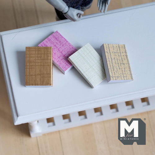 1:12 scale miniature books with blank pages, set of 4 with pink, tan and white fabric look covers, shown on a white table