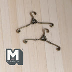 1:12 scale miniature metal clothes hangers in antique bronze with scrolled ends, set of 2, shown on a wood surface