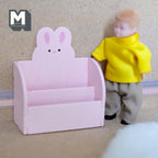 1:12 scale miniature wood bunny 2 tier bookshelf kit in pink with bunny ears back, assembled, beside a boy doll