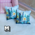 1:12 scale miniature botanical print throw pillows in teal with colorful leaves and flowers, set of 2, on a white rug