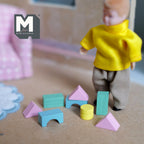1:12 scale miniature wood geometric building blocks, set of 8, teal, pink and yellow shapes shown on the floor beside a doll